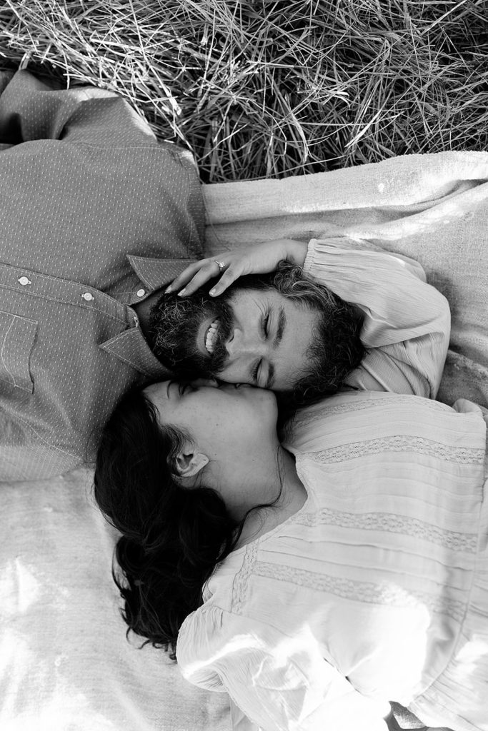 Black and white image of engaged couple's heads together while lying down on a blanket. 