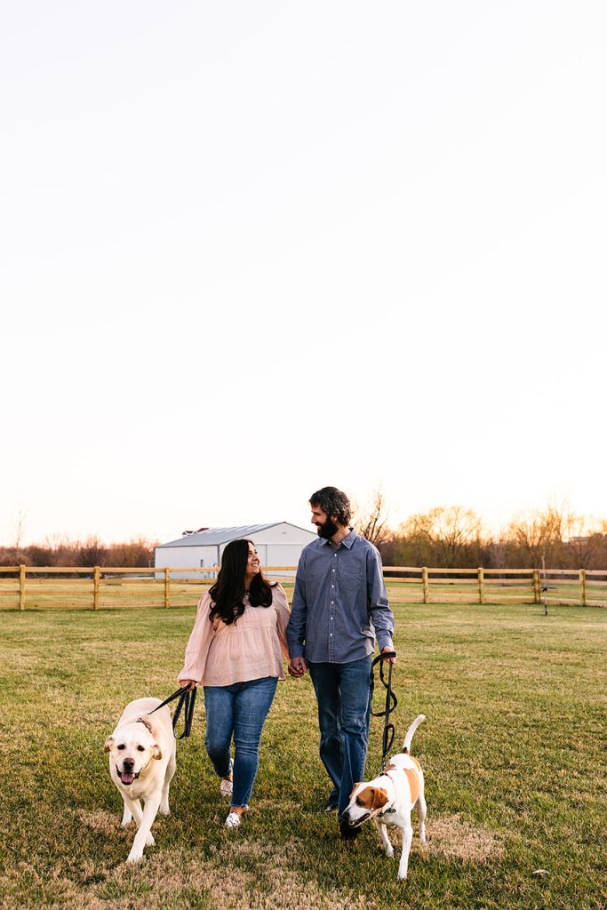 Engaged couple walking towards the camera with their two dogs. 