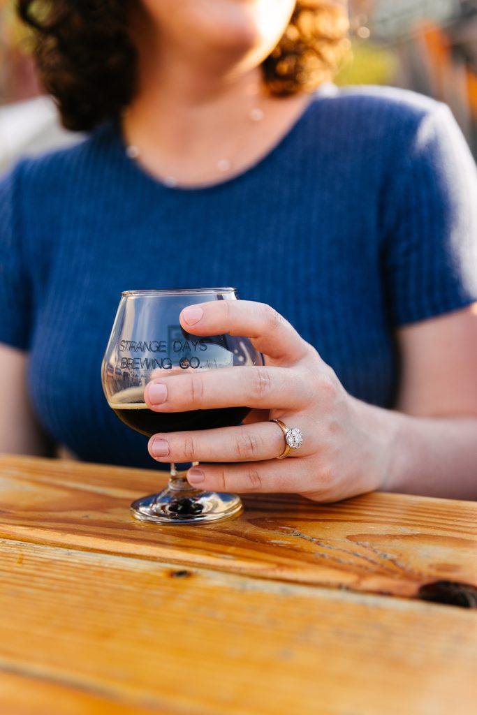 Woman holding a beer from a local brewery with her engagement ring in focus.