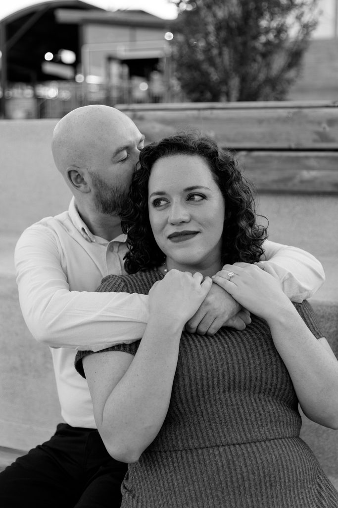 Black and white image of engaged couple sitting & embracing at The Kansas City Rivermarket.