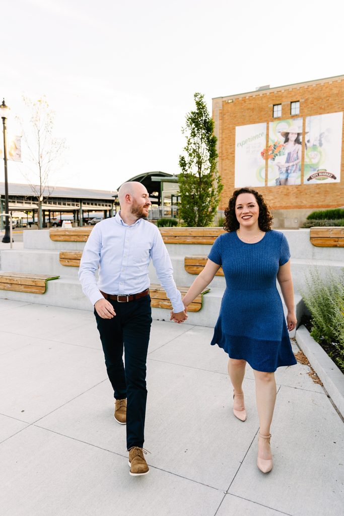 Engaged couple in blue walking towards the camera at the Kansas City Rivermarket.