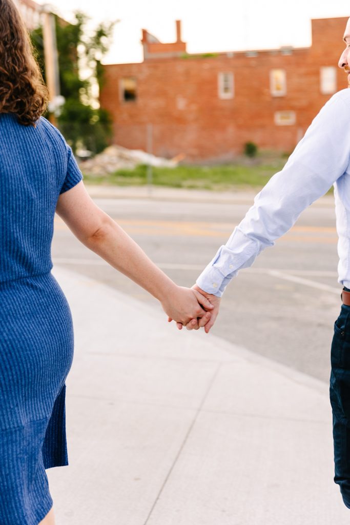 Detail shot of engaged couple holding hands while walking down the street.