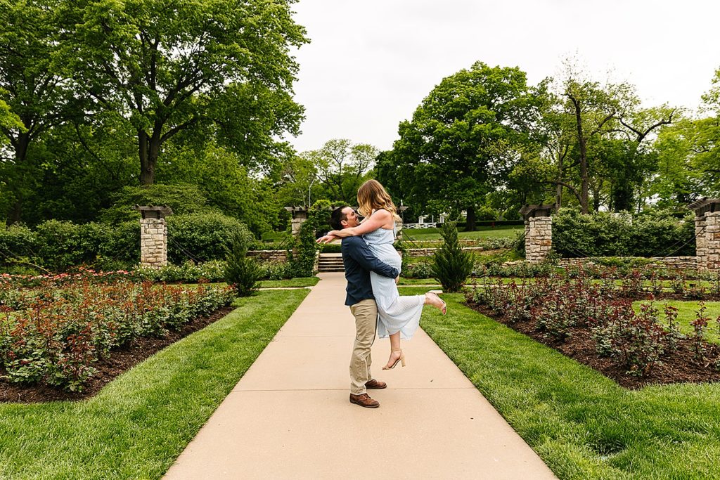 Man holding up woman in the middle of a park for their engagement photo shoot. 