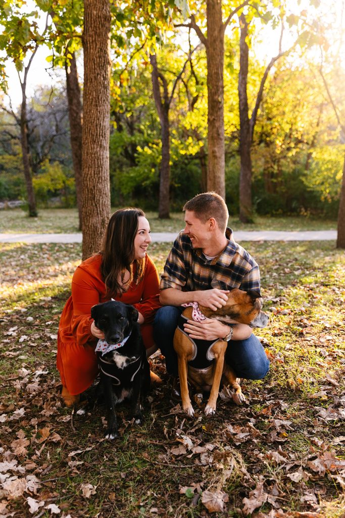 Man and woman kneeling in the park with their two dogs for their engagement photo shoot. 