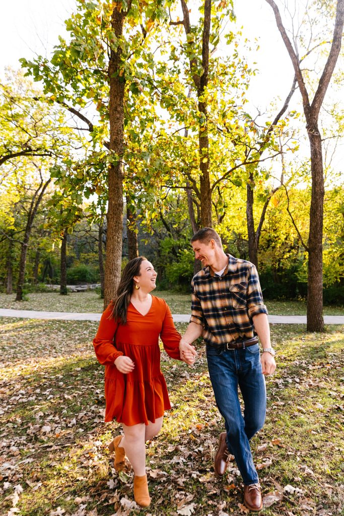 Woman in red dress and man in a plaid shirt running through a park. 