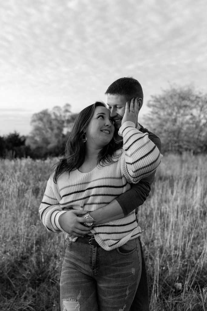Man embracing woman in a field at sunset for their engagement photo shoot with Kansas City Photographer, Natalie Nichole.