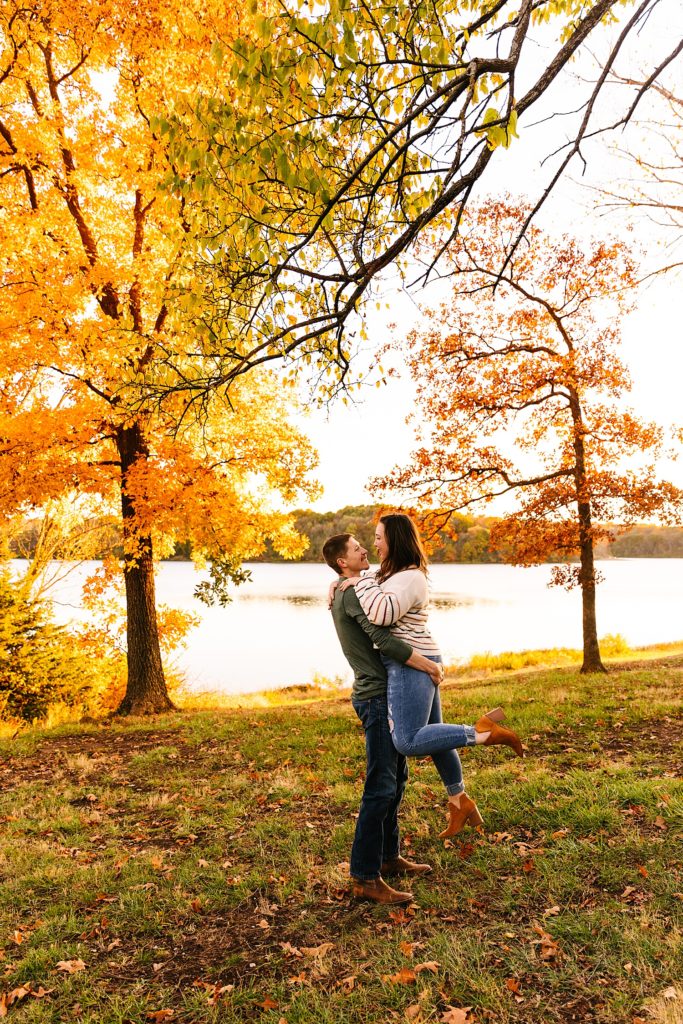 Man lifting up woman with orange trees behind them at their engagement session at Shawnee Mission Park.