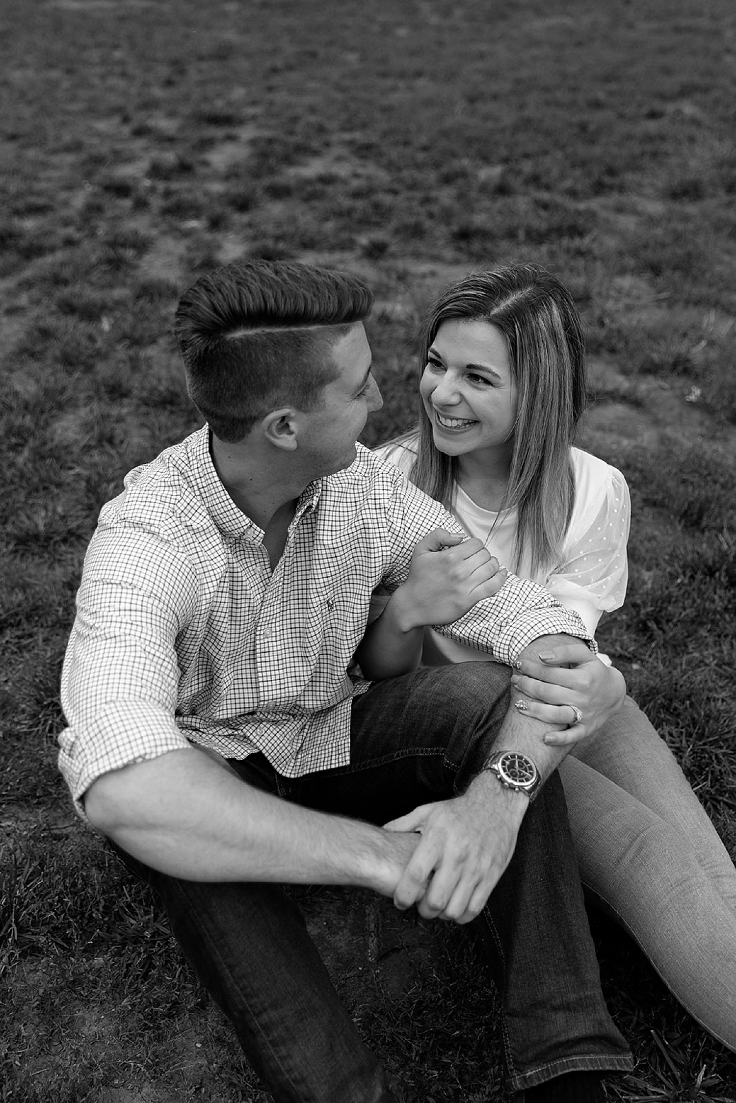 engaged couple sitting in grass field on summer night in Kansas City