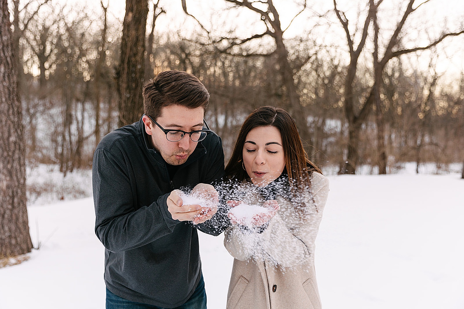 couple playing in snowy shawnee mission park while throwing snow in the air 