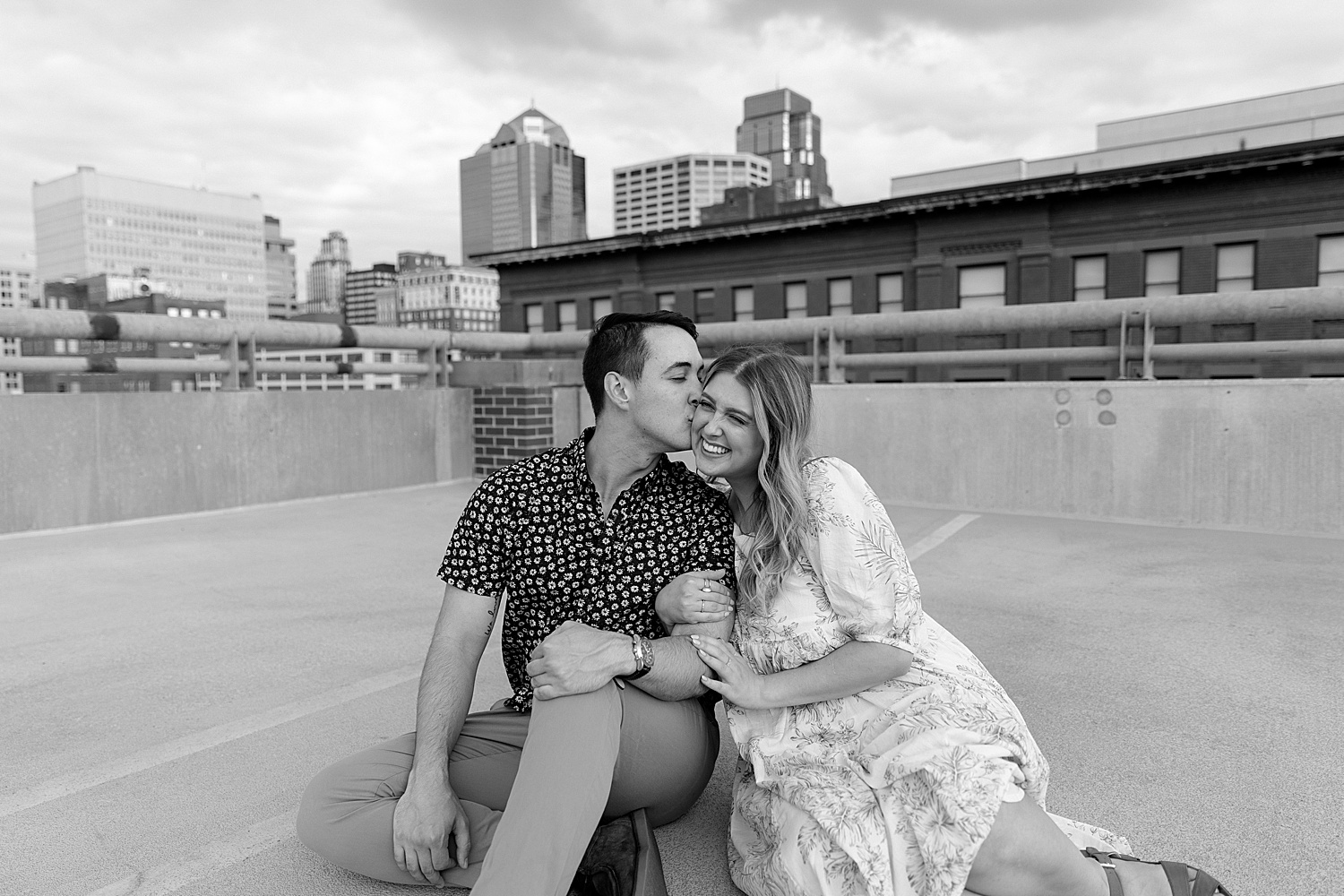 engaged woman smiling while wrapped in fiancés arms on rooftop 