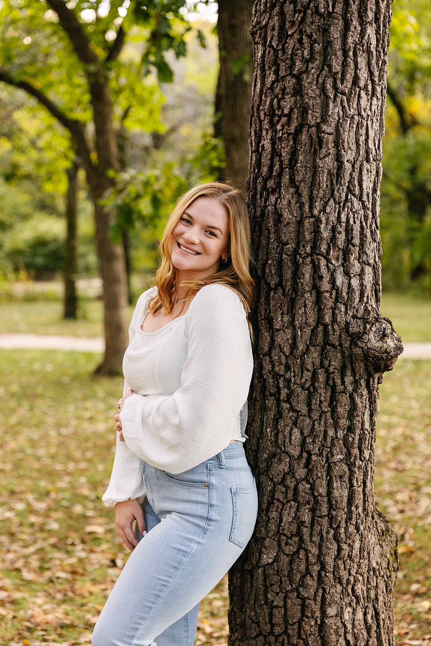 Senior girl standing up against a tree smiling at Kansas senior photographer 