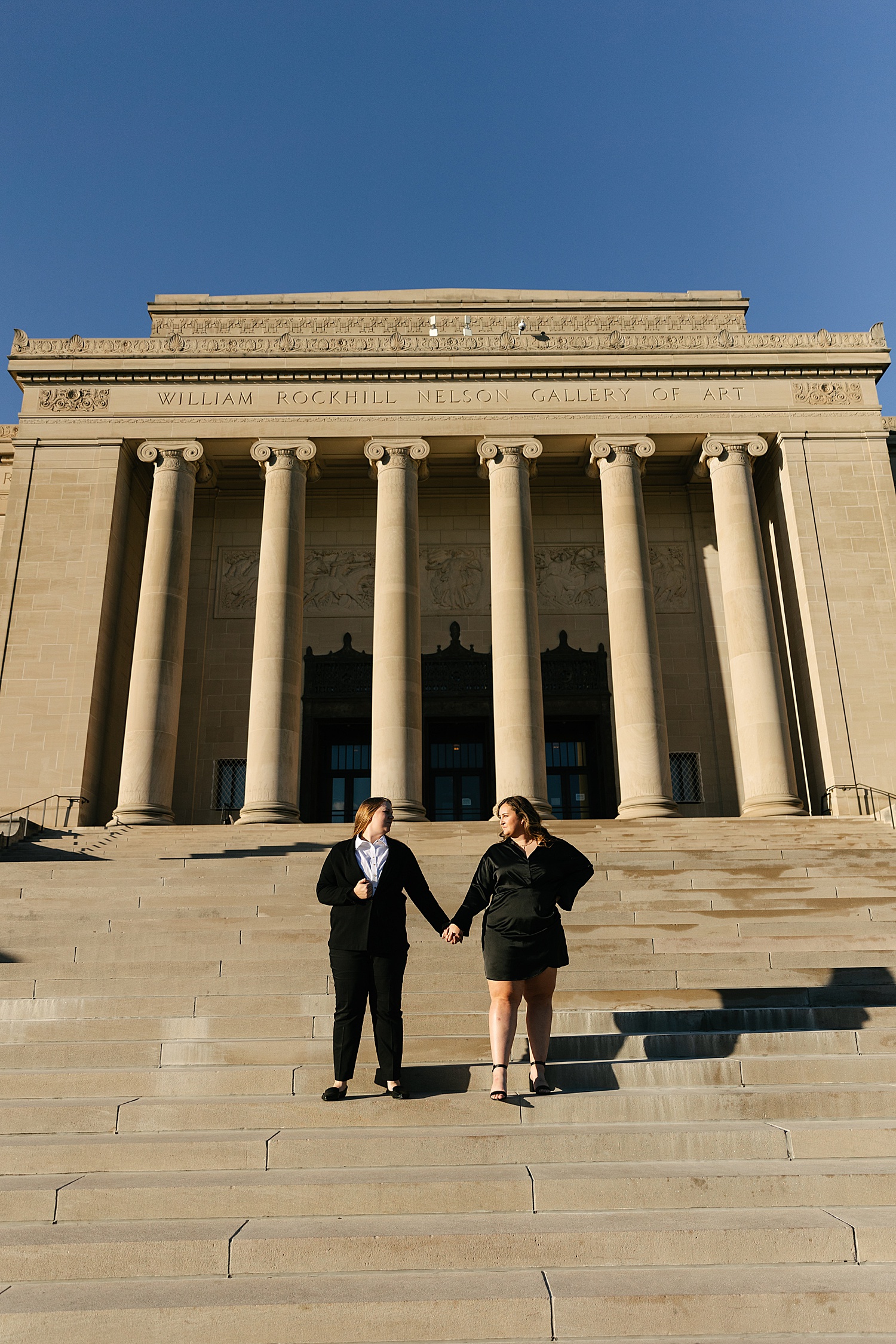 Engaged couple standing on steps of museum during engagement session in Kansas City
