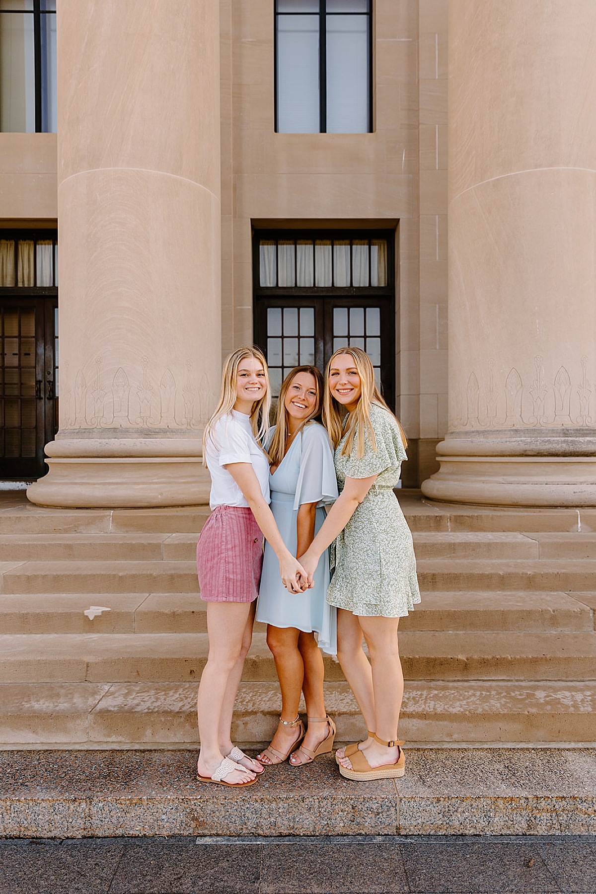 group of three girls holding hands on campus for spring graduation photos 